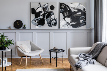 Modern scandinavian home interior of living room with design gray sofa, armchair, marble stool, black coffee table, stylish paintings, decoration and elegant personal accessories in home decor.