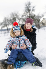 Fototapeta na wymiar Smilling mother and her son sitting in the sledge with a striped cat in the winter garden.