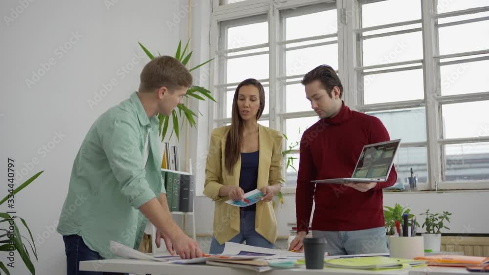 Wall mural medium shot of young startup team of three designers and marketing specialists standing around table
