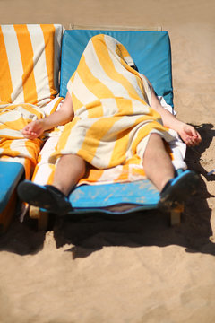 Portrait of a man who put a striped towel over himself not to bake in the sun on the sandy beach