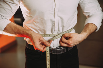 A man in a shirt holds a measuring tape. losing weight