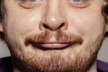Grimaces. Close up of face of beautiful caucasian young man with redhair beard, focus on mouth. Human emotions, facial expression, cosmetology, body and skin care concept. Well kept skin. Wellbeing.