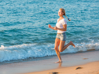Fototapeta na wymiar Smiling adult woman in white T-shirt is jogging on the beach