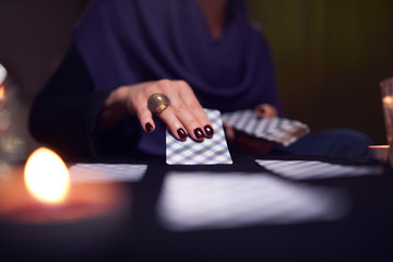 Close-up of female mitt-reader's hands with fortune-telling cards at table with candles