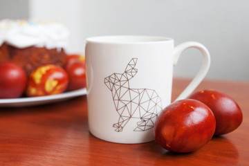 Happy Easter day. White cup with rabbit image amid Easter cake. Morning drink. Easter celebration concept.