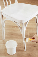 Upcycling concept. Female hand paints with tassel of an old white chair
