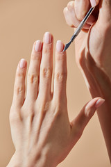 Cropped view of woman doing manicure with cuticle pusher isolated on beige