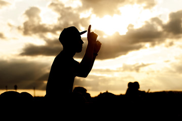 A man in a cap and raised arms takes pleasure at an outdoor music festival. Black silhouette on...