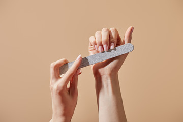 Partial view of woman filing fingernails with emery board isolated on beige - obrazy, fototapety, plakaty