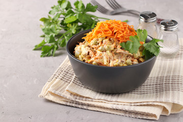 Salad with Korean carrots, meat and canned peas in a dark bowl on a gray background