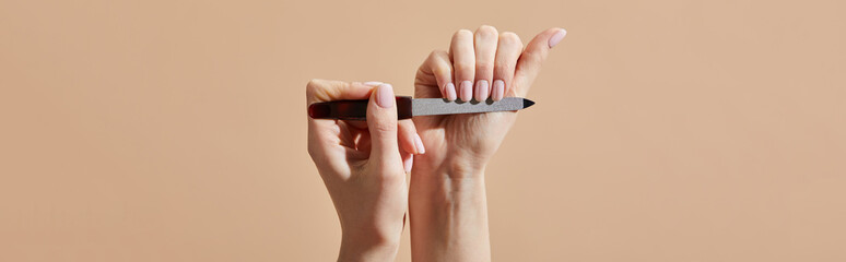 Cropped view of woman filing nails isolated on beige, panoramic shot
