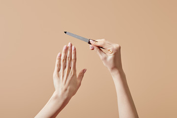 Cropped view of female hands with nail file isolated on beige