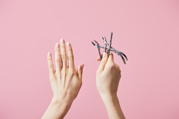 Cropped view of woman holding cuticle pusher and nippers isolated on pink - obrazy, fototapety, plakaty