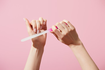 Cropped view of woman filing fingernail with nail file isolated on pink