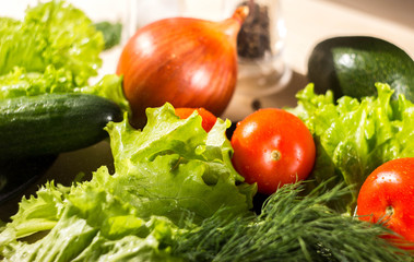 Products for vegetable salad are on a wooden table. Tomatoes, lettuce and cucumbers, on the table