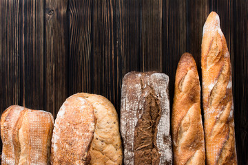 Various kind of bread - gold rustic crusty loaves of bread with wheat on wooden background. Still life captured from above (top view, flat lay).