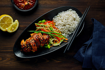 Traditional Japanese teriyaki chicken with salad made of cucumber, ginger, carrot, pepper and cabbage, rice, sesame, edamame, lemon and sweet chili sauce. Top view, directly above.