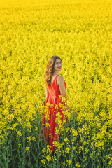 Fototapeta premium Young beautiful girl in a red dress close up in the middle of the yellow field with the radish flowers
