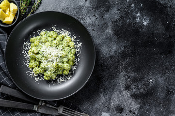 Potato gnocchi  with pesto, parmesan  cheese and spinach. Italian pasta. Black background. Top view. Copy space - obrazy, fototapety, plakaty