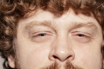 Looks serious. Close up of face of beautiful caucasian young man, focus on eyes. Human emotions, bright facial expression, cosmetology, body and skin care concept. Well kept cheeks. Wellbeing.