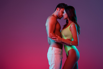 side view of sexy young couple embracing and kissing on purple background with gradient