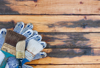 Fototapeta na wymiar Gloves and brushes on old wooden boards. Concept: home repair, house building. Painting tools on wooden floor. Repair your home yourself.