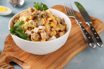 Salad with ham, egg, onion and mushrooms in a white bowl on a wooden board