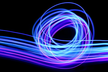 Light painting photography, long exposure photo of purple and blue streaks of vibrant color against a black background