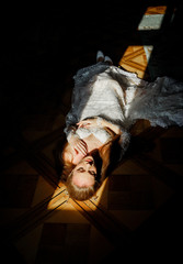 An incredibly beautiful bride lies on the floor with her eyes closed..Rays of light reflect on the floor