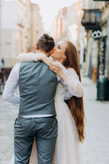 The bride kisses her husband in the ear. Newlyweds walking through the city street.