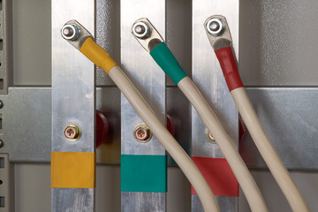 Three electrical cables are connected to a vertical aluminum busbar in the electrical Cabinet. The busbars and the wires marked by color. Busbars are fixed to insulators. Electricity distribution.