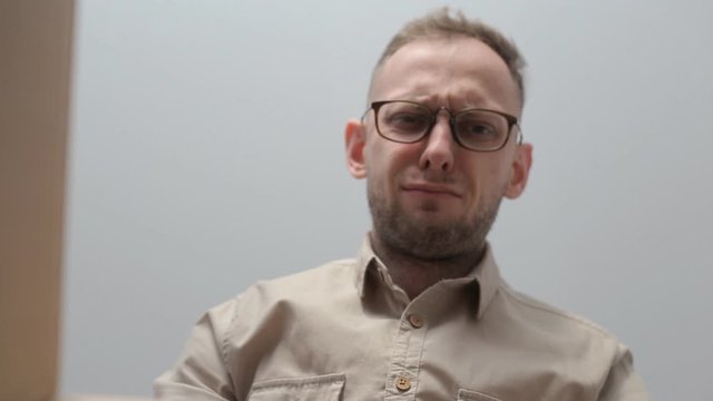 European man with glasses opens a cardboard box and is resent and mutters when he sees what is inside. The concept of dissatisfaction and resent. Shipping and gift. Inside view of the box.