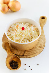 Sauerkraut with a wooden spoon and pepper on a white table. Fermented food concept.
