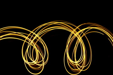 Light painting photography, long exposure photo of loops of gold metallic abstract color against a black background
