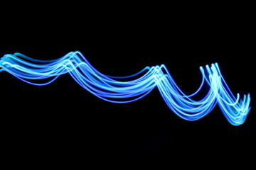 Long exposure photograph of neon blue streaks of light in an abstract swirl, parallel lines pattern against a black background. Light painting photography.