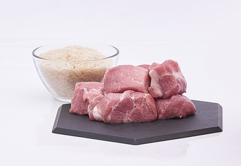 pork pieces raw and rice on black plate