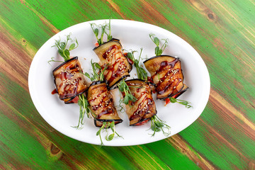 Eggplant vegetable rolls with unagi sauce. On a colored wooden background. Vegetarian dish.