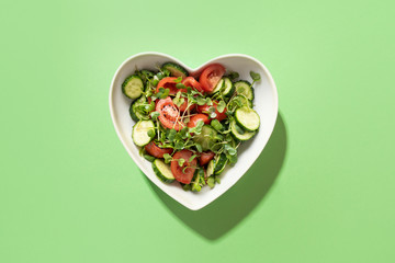 Fresh salad with tomato, cucumber, vegetables, microgreen radishes in plate shape of heart on...