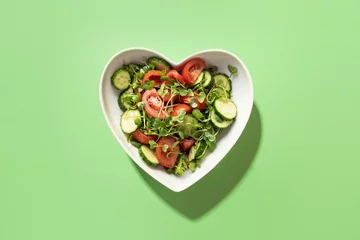 Foto auf Glas Frischer Salat mit Tomaten, Gurken, Gemüse, mikrogrünen Radieschen in Plattenform des Herzens auf Grün. Sicht von oben. Konzept vegan und gesunde Ernährung. © svetlana_cherruty