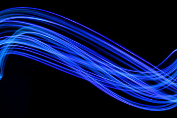 Long exposure photograph of neon blue streaks of light in an abstract swirl, parallel lines pattern against a black background. Light painting photography.