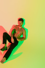high angle view of sexy shirtless man in black jeans lying on yellow with red and green shadows