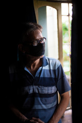 Obraz premium Portrait of an Indian old man wearing corona preventive mask in home isolation in front of a window. Indian lifestyle and disease.