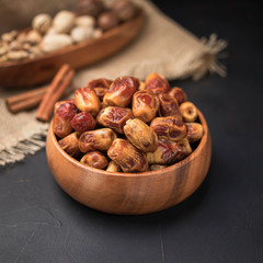 dried fruit in a square wooden bowl on a dark background and burlap