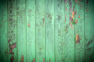 Background in grunge style. Wooden old fence with peeling paint. From vertical boards of turquoise color. With dark vignette around the edges.