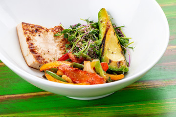 Fried tofu with grilled avocado and wok vegetables. On a colored wooden background. Vegetarian dish.