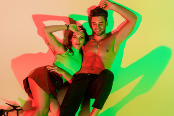 Obraz na płótnie Canvas sensual, trendy girl and sexy man smiling while lying on yellow background with red and green shadows