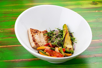 Fried tofu with grilled avocado and wok vegetables. On a colored wooden background. Vegetarian dish.