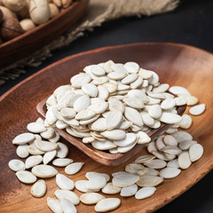 nuts on a square wooden bowl and an oval wooden tray on a dark background and burlap