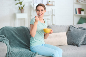Obraz na płótnie Canvas Young woman eating tasty yogurt at home