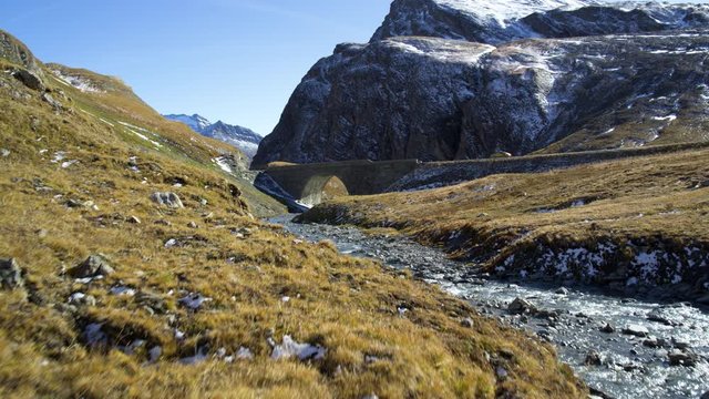 Amazing yellow sport car Porsche riding on beautiful mountain road and stone bridge surrounded by the mountains in snow and rocky river 